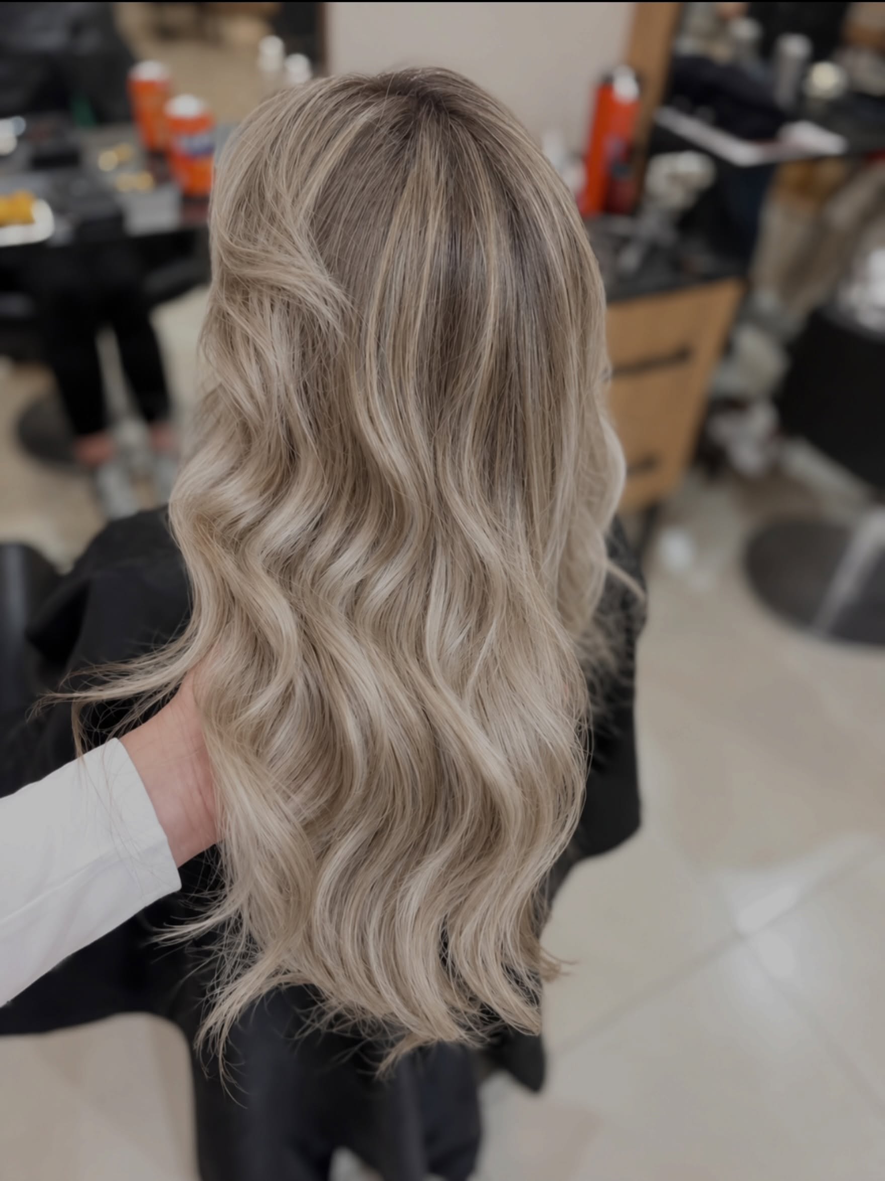 Lange asblonde balayage-golven van achteren in de salon